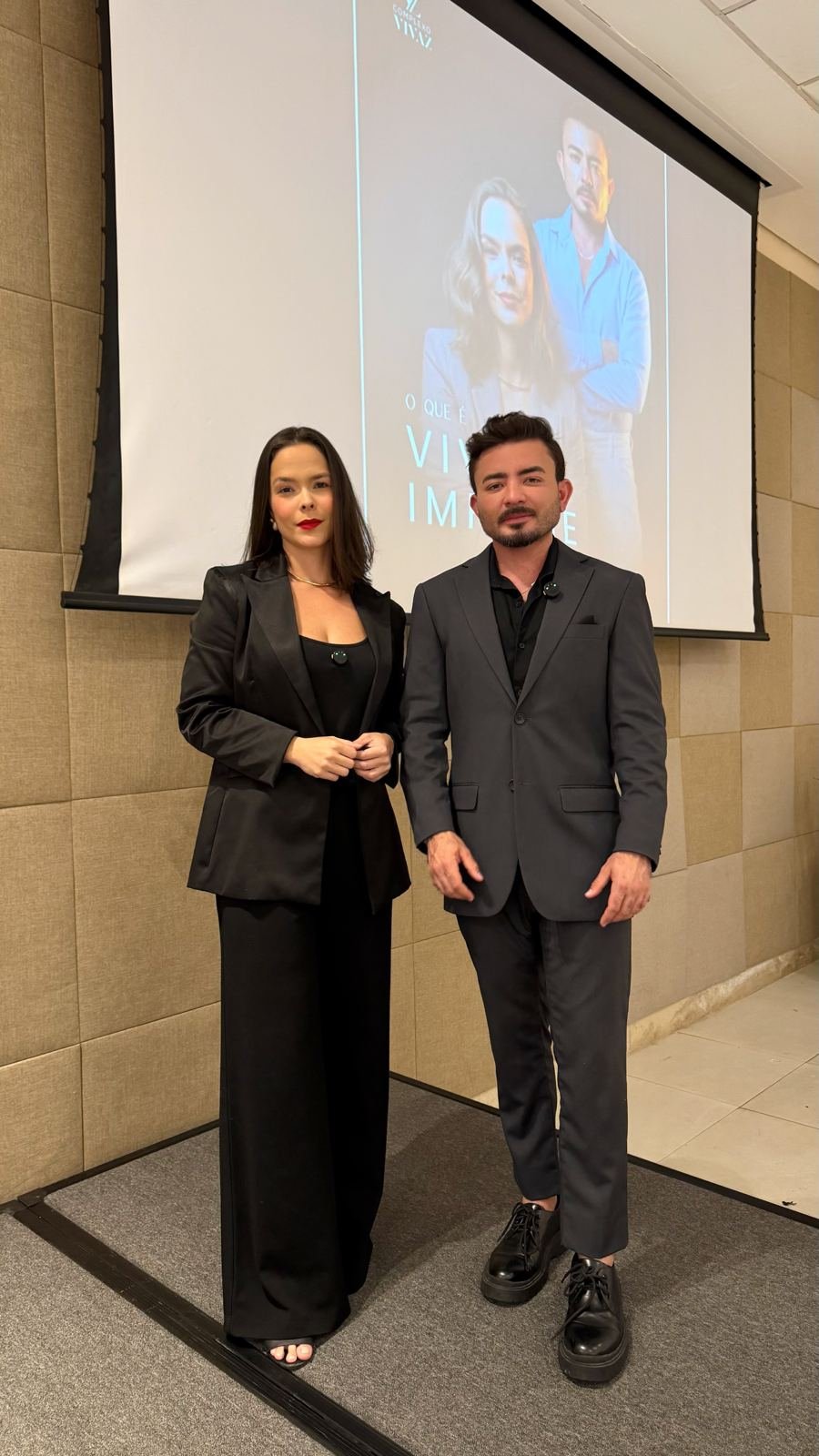 Dra. Caroline Mota e Dr. Ítalo Cavalcante em frente ao telão do Vivaz Impulse